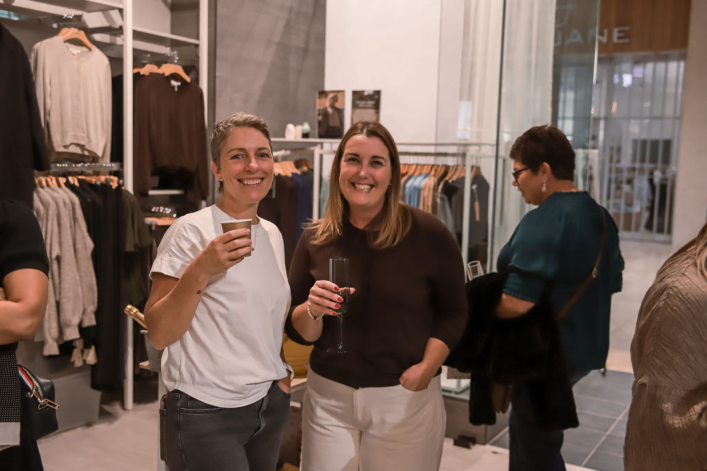 Two attendees smiling with drinks at the MAX Fashion evening