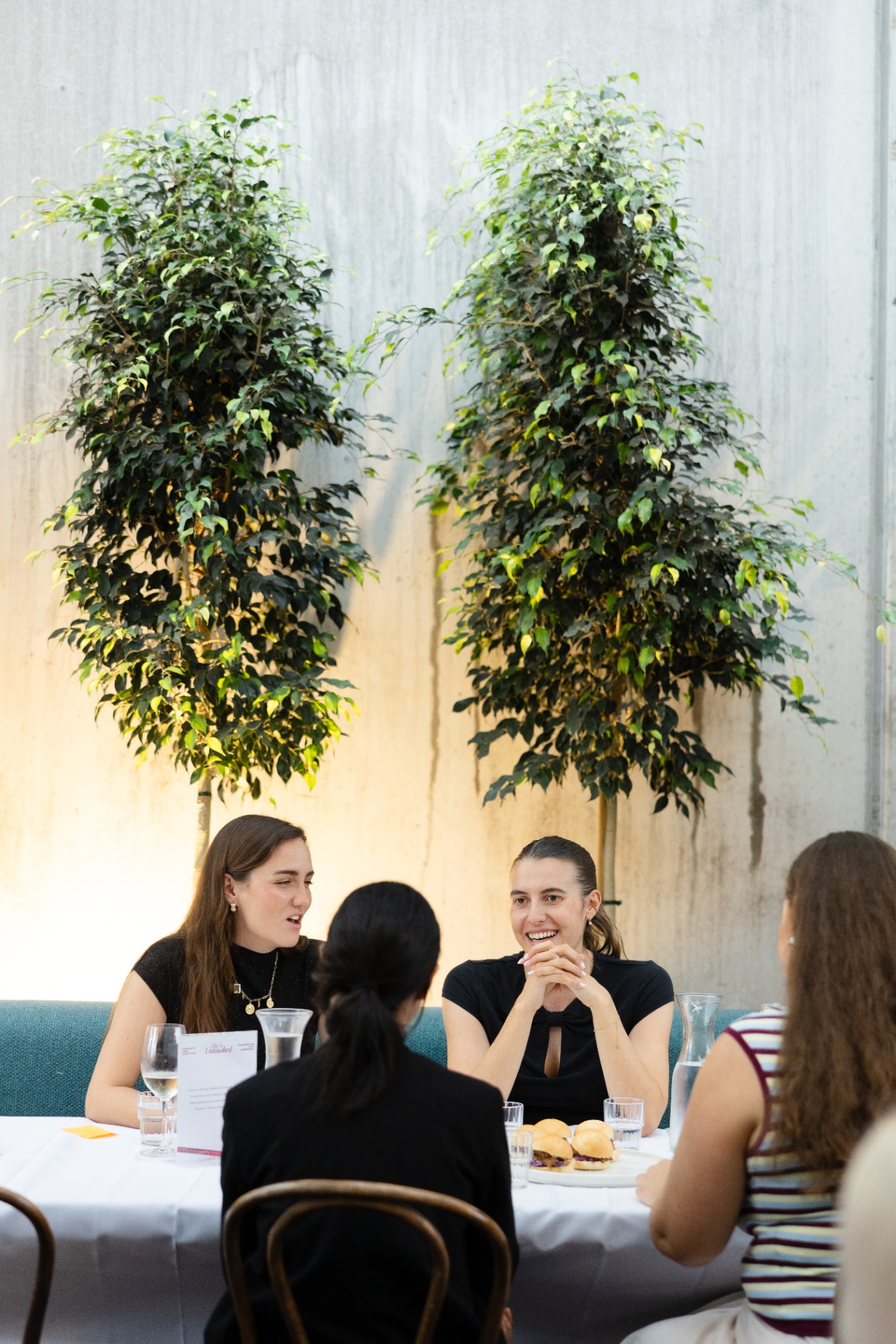 Women gathered around the table beneath the tall indoor trees