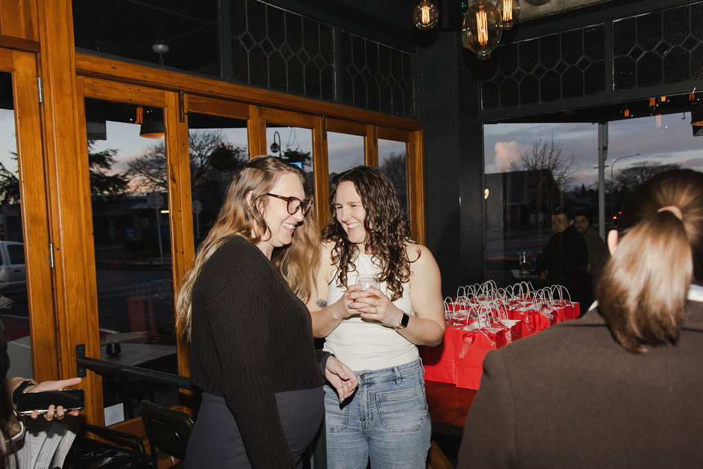 Guests chatting by the windows at golden hour with red goodie bags behind them