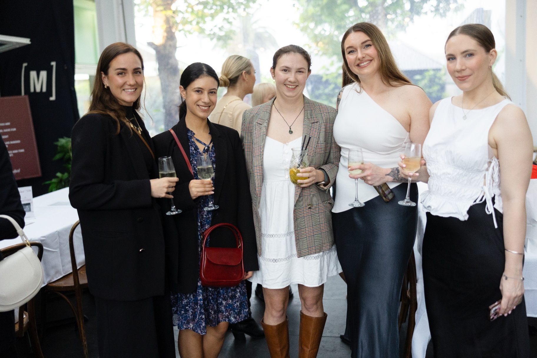 Five guests smiling together with drinks in hand